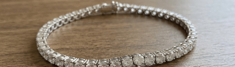 Diamond tennis bracelet with heart-shaped charm engraved 'R + E' on gray cushion